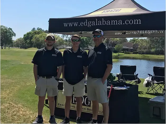 3 men standing in front of a booth for engineering design group on a golf course